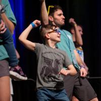 An action shot of a young boy and other dancers flexing their biceps.