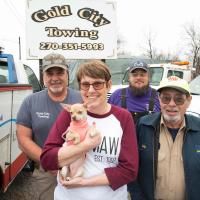 Debbie holds her chihuahua and smiles for a group photo with her family at the Gold City Towing yard.