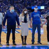 Andy, Julie, and three of his doctors stand in a line and hold hands while standing on the half-court line at a UK basketball game.