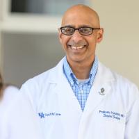 Dr. Prakash Pandalai, an older South Asian man with a bald head, smiles as he talks with a female colleague who has her back turned to the camera.