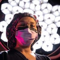 Dr. Capoor prepares for surgery with her hair net and face mask on in front of an operating table lamp.