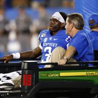 Terry rides in the back of a golf cart off of the field after sustaining his injury. He is accompanied by a trainer, his facial expression is grim.