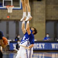 An action shot of Travis holding up another cheerleader as she stands on his hands during a basketball game.
