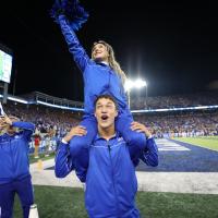 Travis cheers at a UK Football game, while a female cheerleader sits on his shoulders.