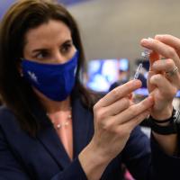 Dr. Montgomery-Yates, wearing a facemask, pulls a dose from a vial of vaccine.