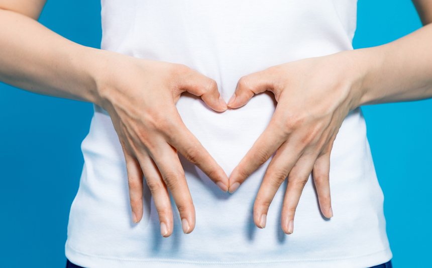 A woman forms the shape of a heart with her hands over her belly.