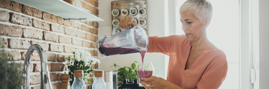 A woman in her kitchen pours a smoothie from a blender.