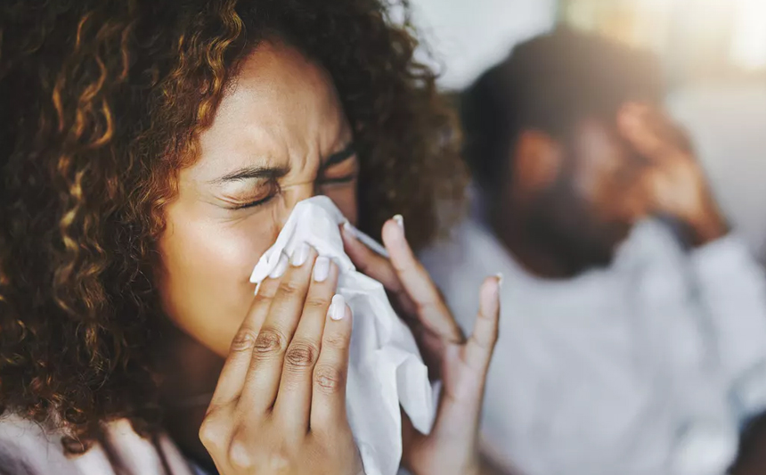 A woman suffering from allergies sneezes into a tissue.