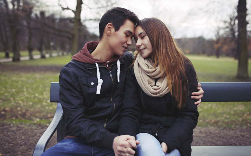 A teenage couple seated on a park bench.