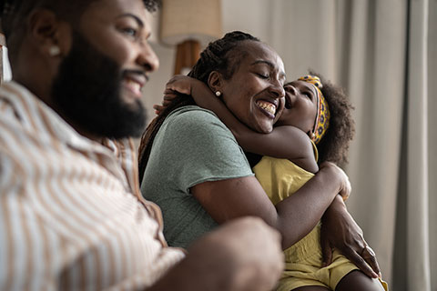 Little girl embraces her mother while her father sits next to them both, smiling
