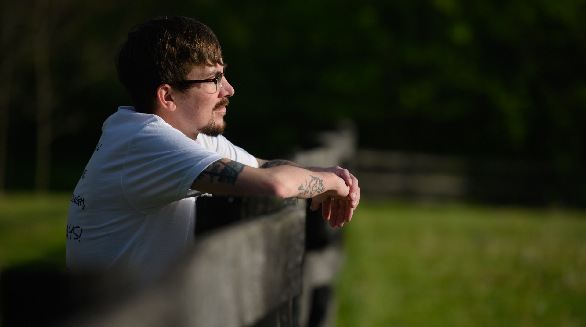 Cameron stands turned to his side, with his hands on the border fence of the park as he stares into the horizon.