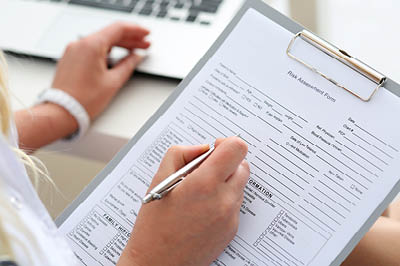 A person with long blonde hair uses a pen to complete a form that's attached to a clipboard. The photo is a closeup of the individual's hands.