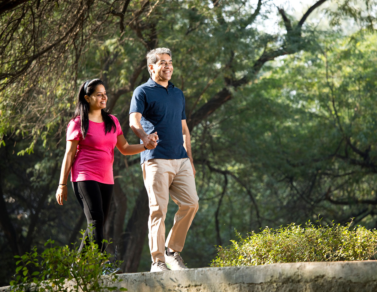 A man and woman, in their 40s or 50s, walk through a wooded area, possibly a park.