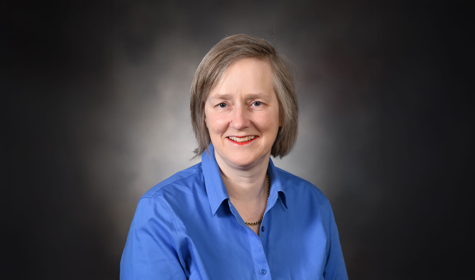 Dr. Emma Birks, smiling toward camera, dressed in a blue shirt