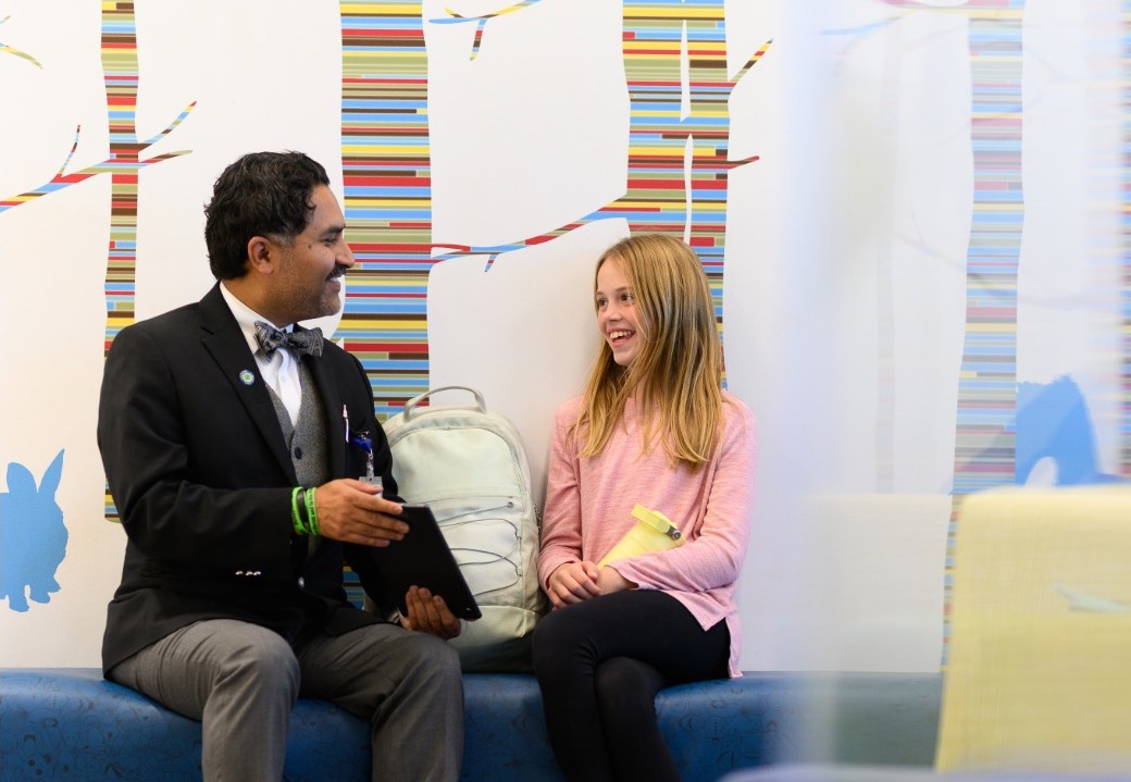 Dr. Qaiser sits down on bench and converses with young child 