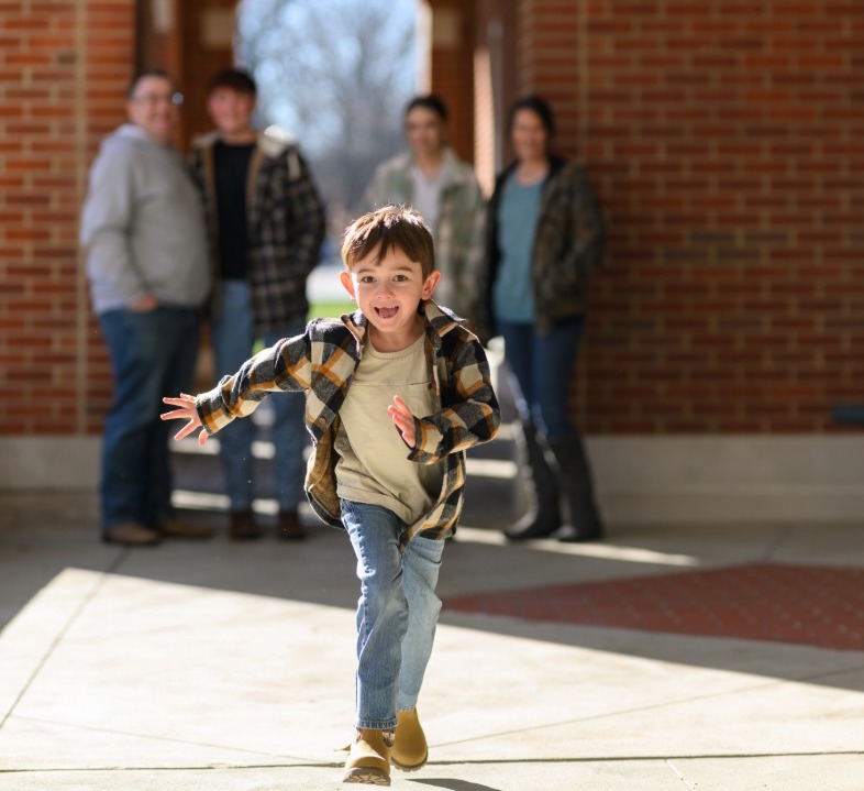 Small boy runs towards the camera while family stands behind him