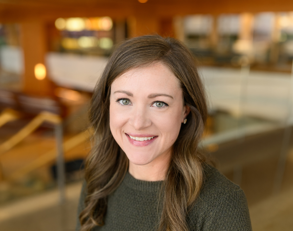 Katie Brown against a blurred background; she's wearing a brown sweater