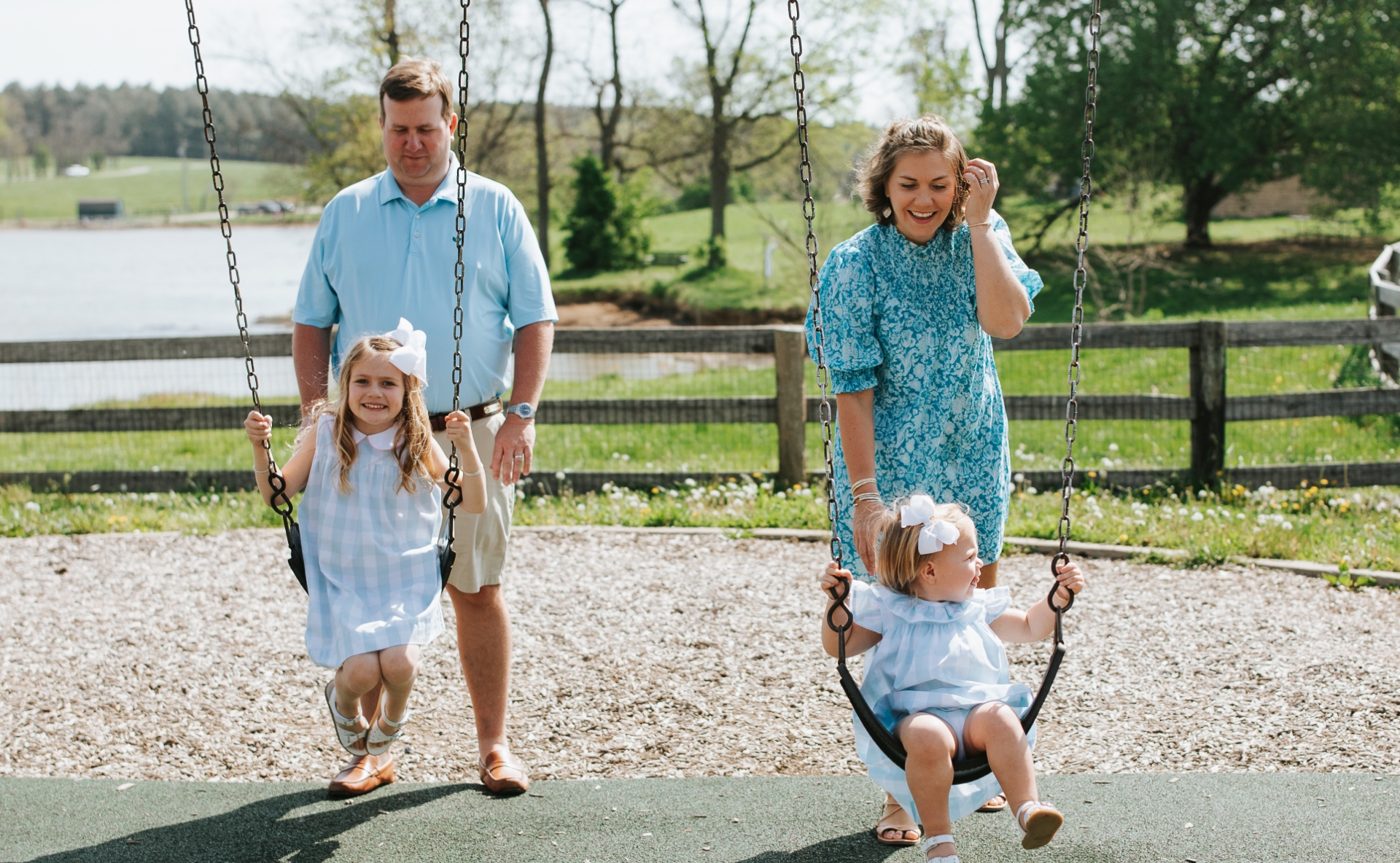 A candid photo of Anne Sydney and Jesse pushing their daughters on the swing set.