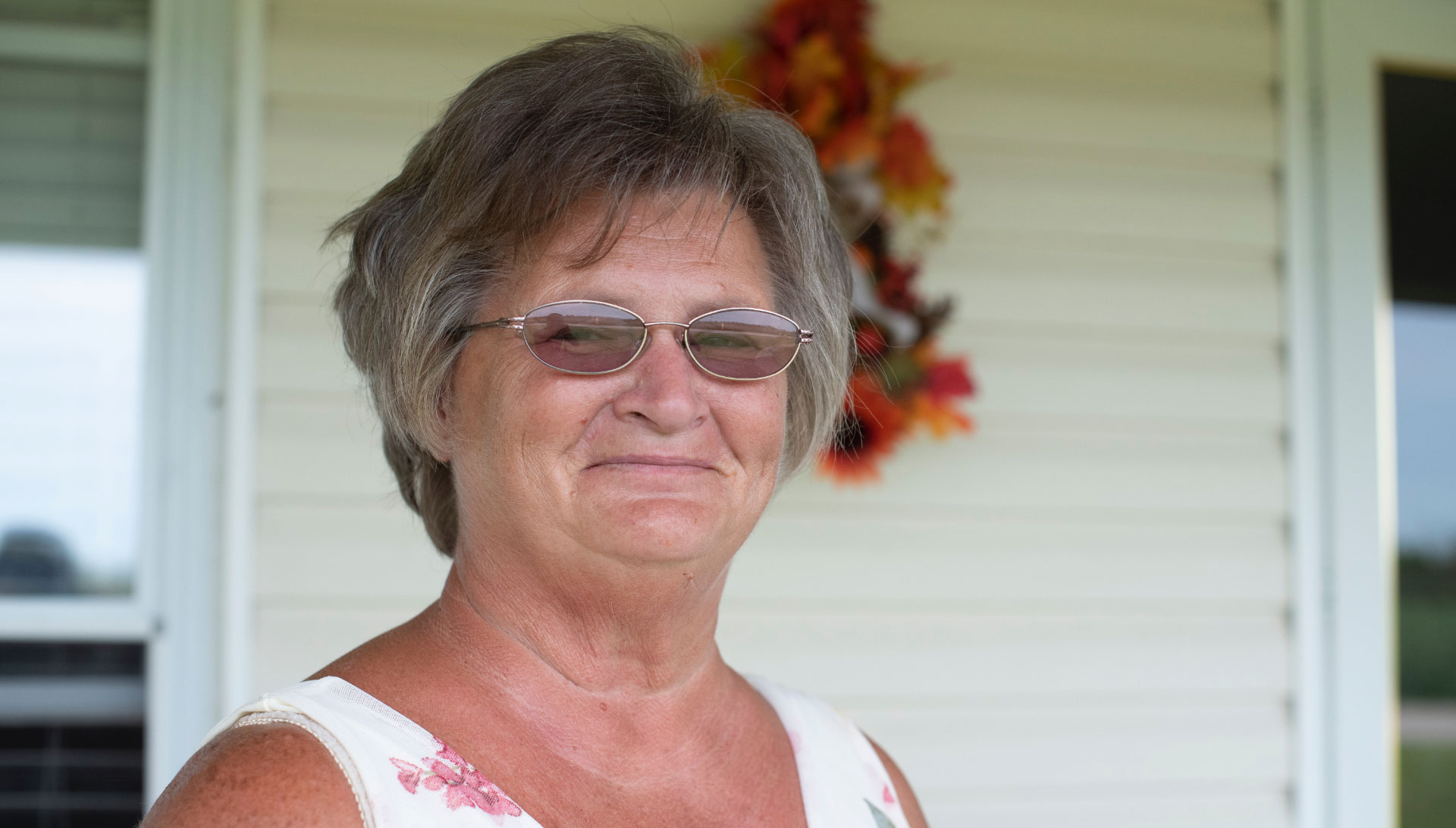A portrait of Charlotte, a woman in her late sixties with glasses and short hair, smiling slightly at the camera.