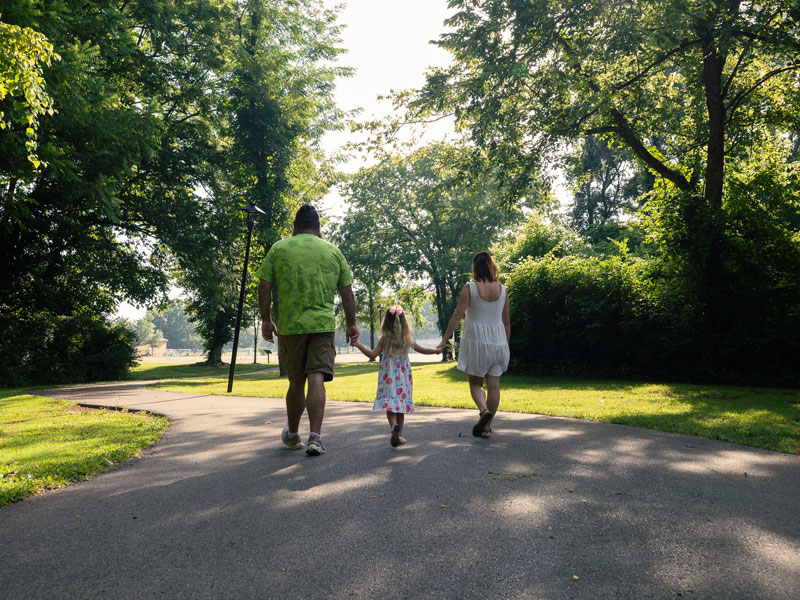 Joshua Newton, Izzy Newton and Jamie Newton photographed from behind as they walk on a park track holding hands