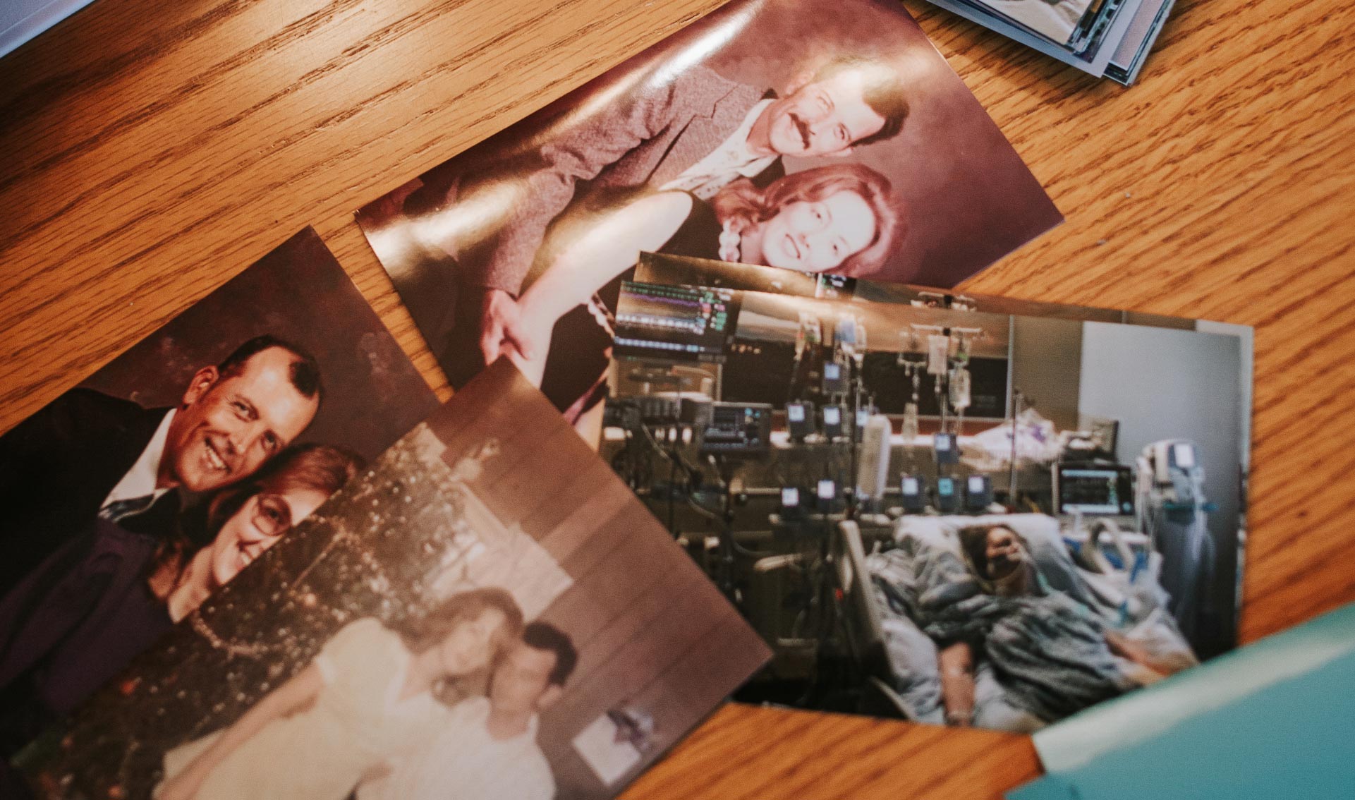 Four photographs are spread out on a table. Pictured in three of the photographs are Mae and her husband, Bobby, in their earlier years, posed in a warm embrace and standing close to one another. The fourth image is captured in a hospital room, with an individual attached to several machines, laying in a hospital bed.