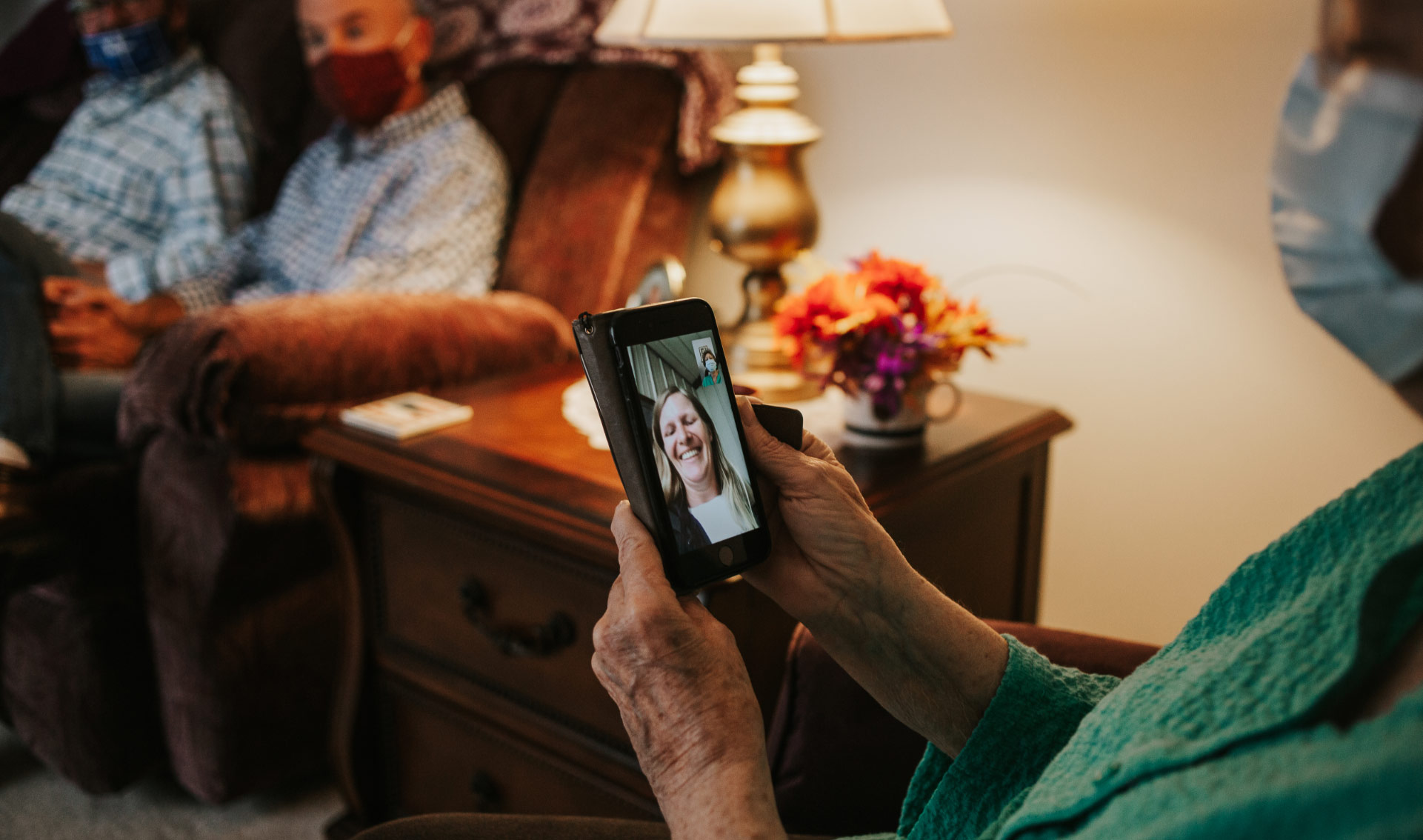 A close-up of Mae wearing a mask at home, on a video call with a young white woman who is smiling widely.