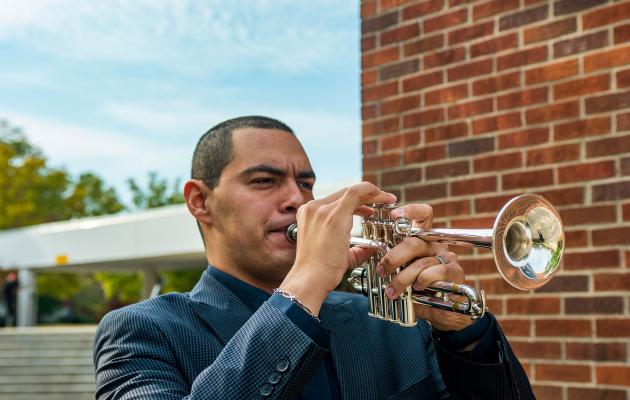 Adiel Nájera plays his trumpet while standing outside on the University of Kentucky campus. 