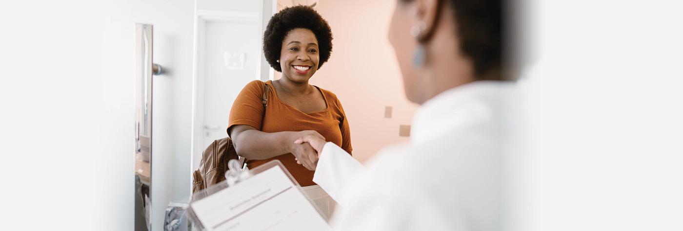 An African-American woman shakes hands with her provider, who we see from over her shoulder, at the beginning of an appointment.