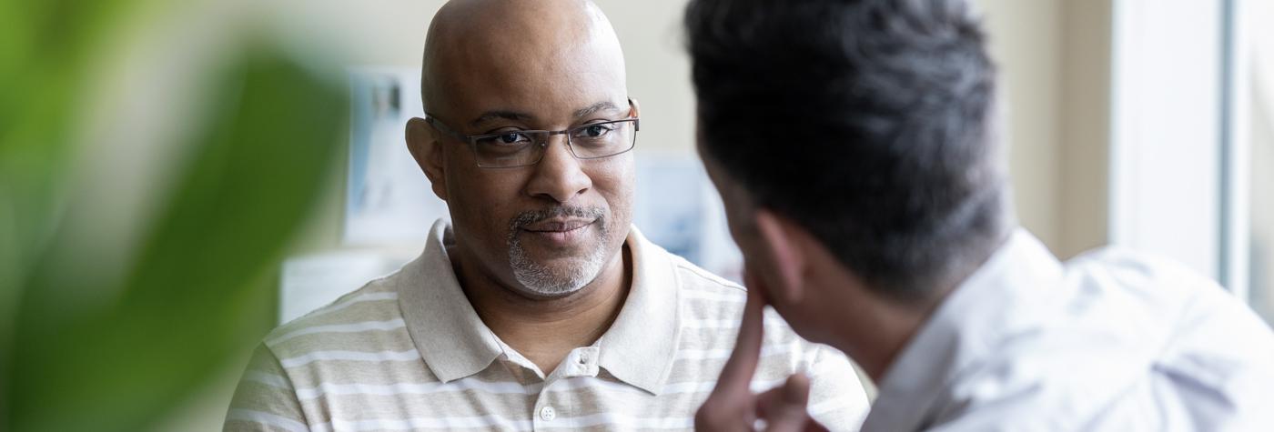 A middle-aged African-American man has a conversation with his doctor, a man whom we see from behind.