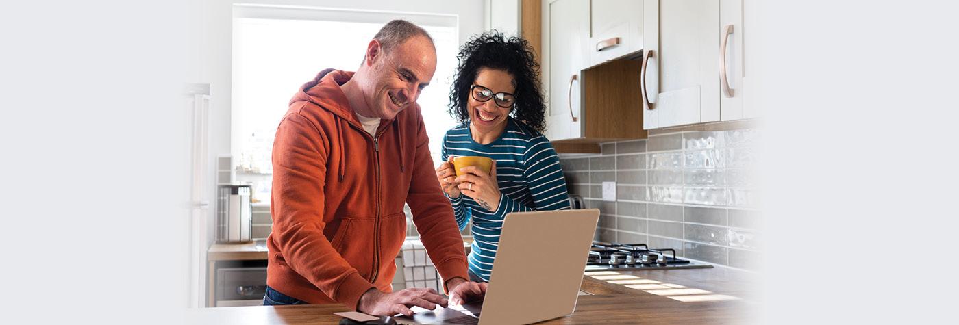 A man and woman stand side by side and look at information on a laptop computer.