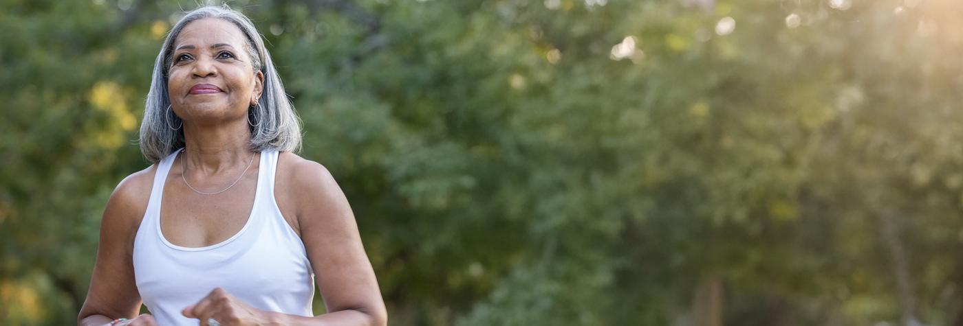 A woman wearing a white tank top walks outdoors, smiling softly.