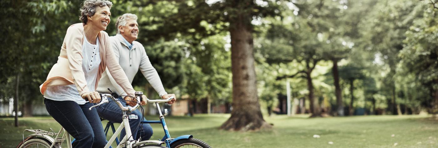 A couple rides bicycles side by side through a park. 