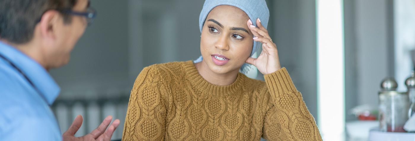 A young woman wearing a gold sweater and light blue headwrap speake with a man wearing a light blue shirt.