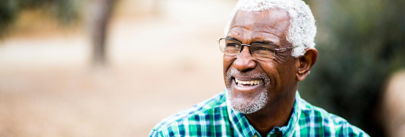A smiling, older man wearing a green and blue plaid shirt