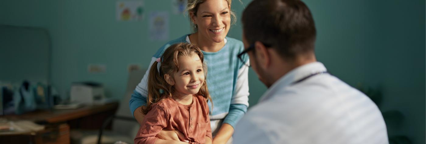 A mother and little girl smile while talking to a doctor. 