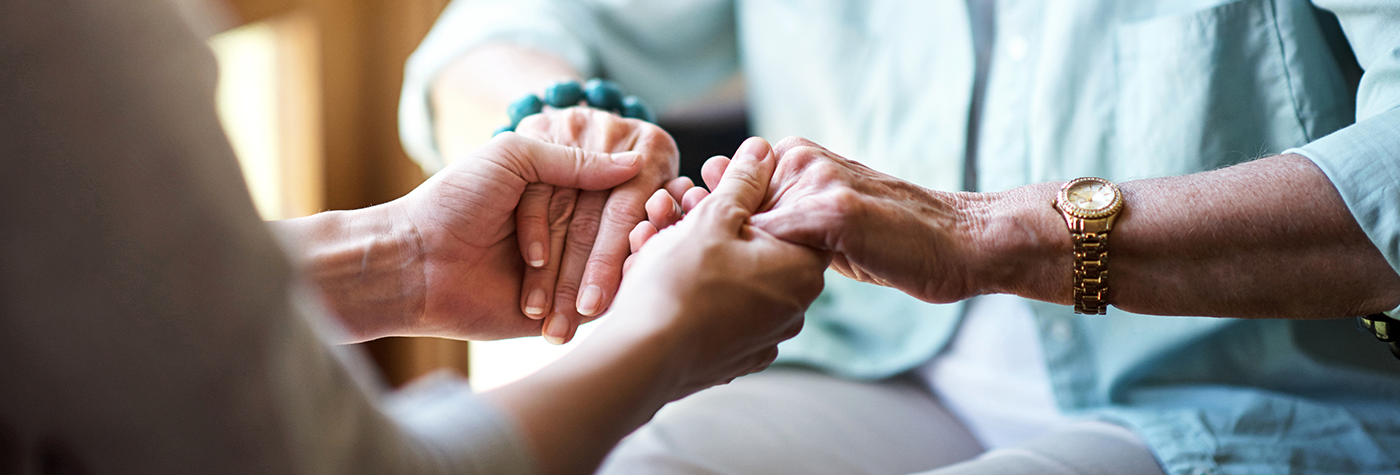 Close-up of two people seated indoors, showing one person holding another person’s hands in a supportive gesture.