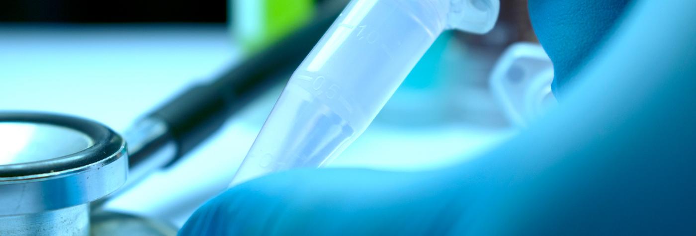 Gloved hand holding a small microcentrifuge tube in a lab setting.