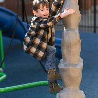 Granger Smith, smiling toward the camera, climbs a small playground fixture shaped kind of like a rock
