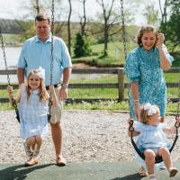 A candid photo of Anne Sydney and Jesse pushing their daughters on the swing set.
