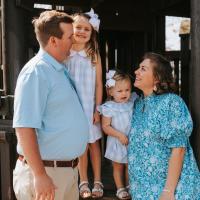 A candid photo of the Parrish family smiling at each other as they stand in front of a structure at the playground.