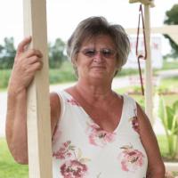 A portrait photo of Charlotte, dressed in a white tank top with pink flowers, standing on her porch.
