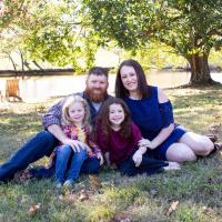 Izzy's family sits on the ground together for a family photo.