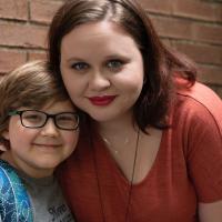 A photo of Ellie and her mom, Morgan, a young looking woman with brown hair wearing red lipstick and an orange shirt. Morgan’s arm is around Ellie’s shoulders. Both are smiling.