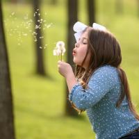 Henley stands in a park blowing a handful of dandelions.