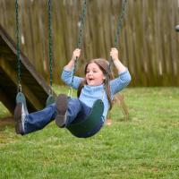 Henley smiles as she swings back and forth on a playground.