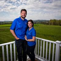 Jacob and his wife Allison lean against their porch railing and smile for a photo.
