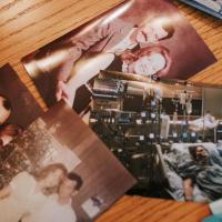 Four photographs are spread out on a table. Pictured in three of the photographs are Mae and her husband, Bobby, in their earlier years, posed in a warm embrace and standing close to one another. The fourth image is captured in a hospital room, with an individual attached to several machines, laying in a hospital bed.