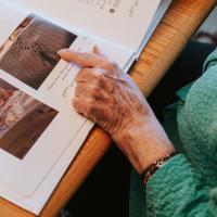 Mae is flipping through a photobook, pointing to a picture her grandchildren drew.