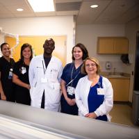 Margie stands and smiles for a photo with a group of nurses next to a CT scanning machine.