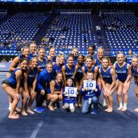 Izzy and Dalton hold signs with 10's on them and kneel in front of a group of UK gymnasts.